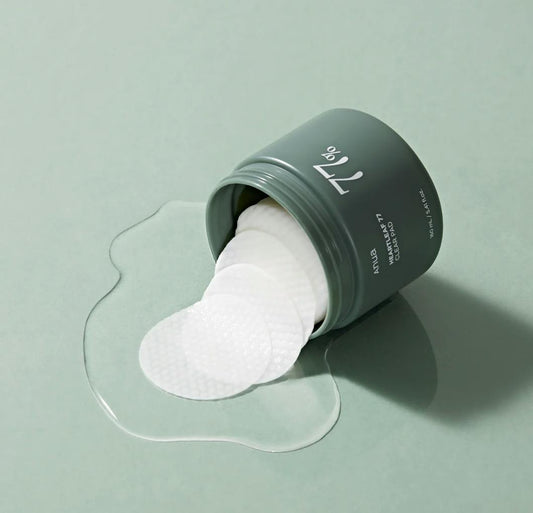 ANUA Heartleaf 77% Clear Pad jar with pads spilling out and liquid on a green background.