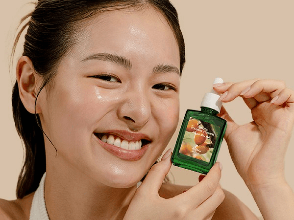 Smiling woman holding Dr.Althea Gentle Vitamin C Serum, showcasing its revitalizing benefits for healthy skin.
