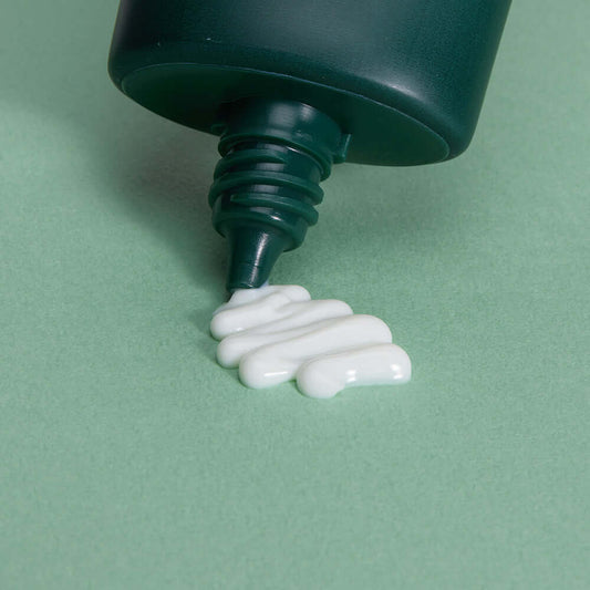 ANUA Heartleaf Silky Moisture Sun Cream being squeezed out of a green tube on a green background.