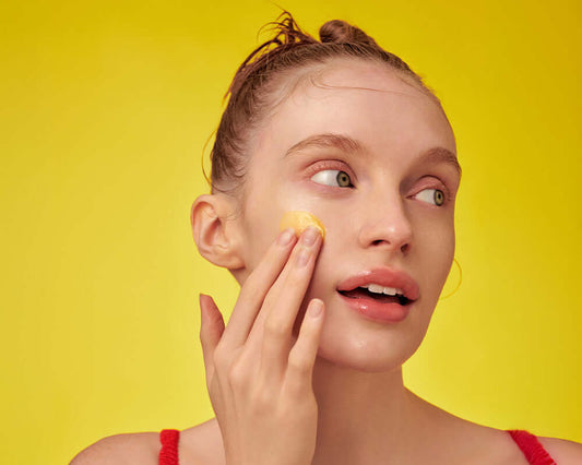Model applying EQQUALBERRY Vitamin Illuminating Serum on her face with a bright yellow background.
