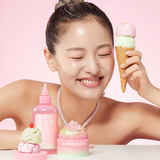 Smiling woman enjoying APRILSKIN Pink Aloe Pack Cleanser with ice cream, showcasing beauty and skincare products in a vibrant setting.
