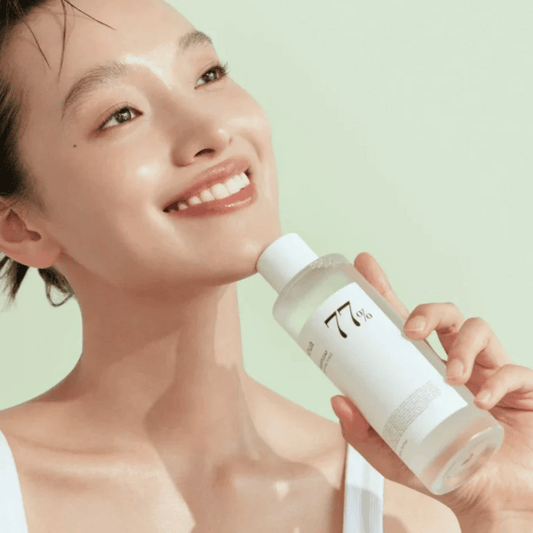 Model holding ANUA Heartleaf 77% Soothing Toner with a radiant smile against a light green background.