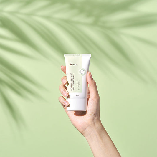 iUNIK Centella Calming Daily Sunscreen SPF 50+ PA++++ held in hand against a green background.