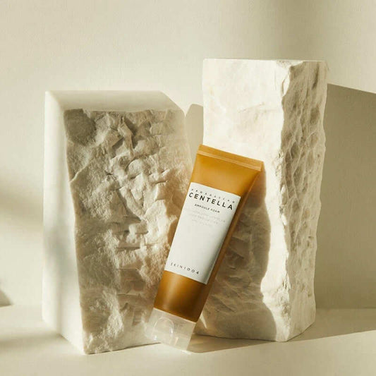 Skin1004 Madagascar Centella Ampoule Foam cleanser in elegant packaging beside textured stone blocks, showcasing a calming skincare product.