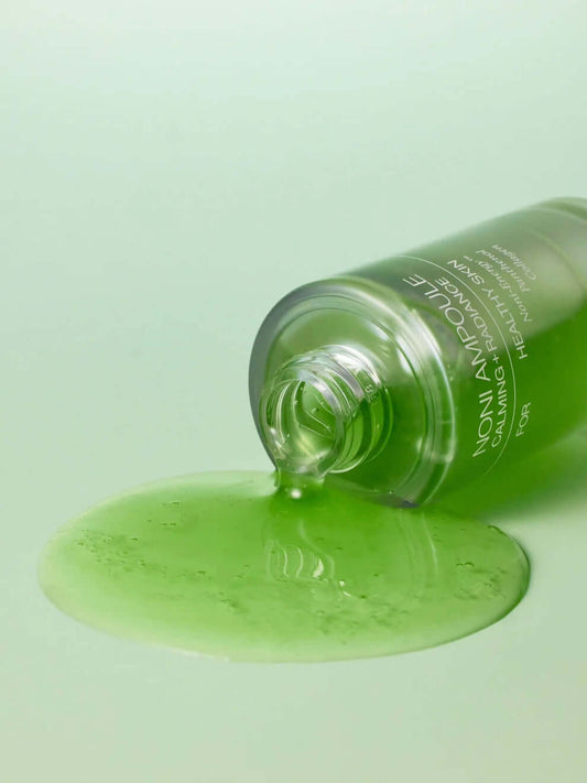 Celimax Noni Energy Ampoule 30ml, soothing green serum spilling from bottle on a pale green background.