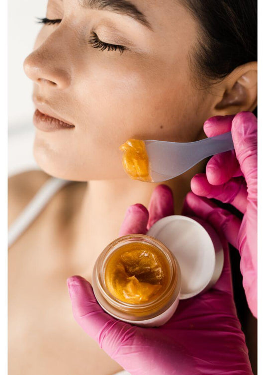 Woman receiving facial treatment with golden cleansing balm during Korean skincare routine.