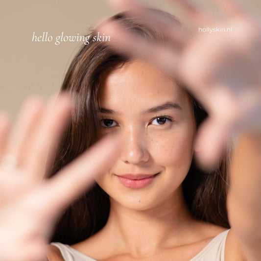 A woman with glowing skin, smiling and posing with her hands near her face for a skincare promotional image.