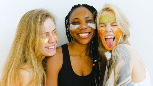 Three women smiling with colorful face masks, showcasing skincare rituals and the joy of self-care.