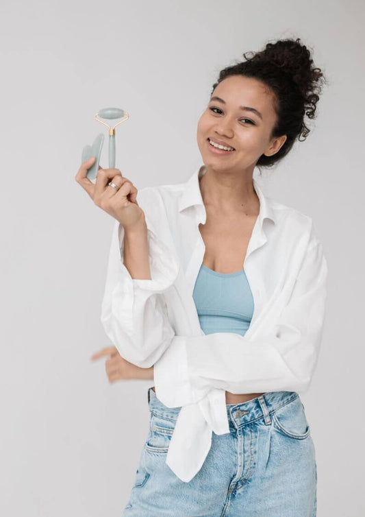 Smiling woman holding a skincare jade roller, showcasing K-beauty trends in casual attire.