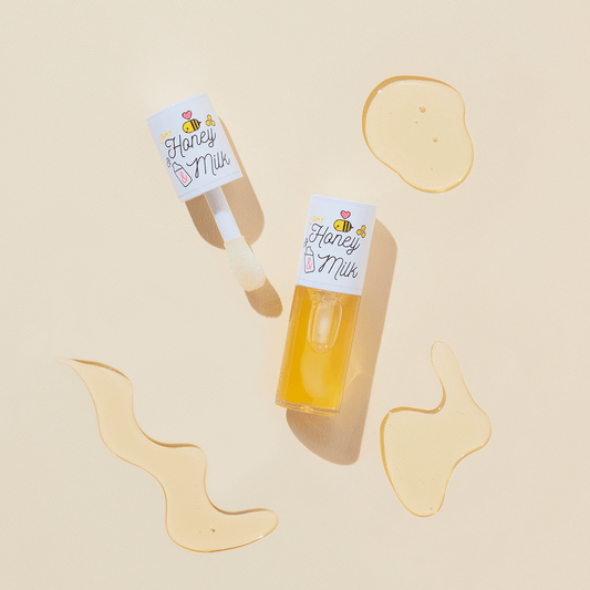 A'pieu Honey&Milk Lip Oil bottle with applicator and honey-like droplets on a creamy background.